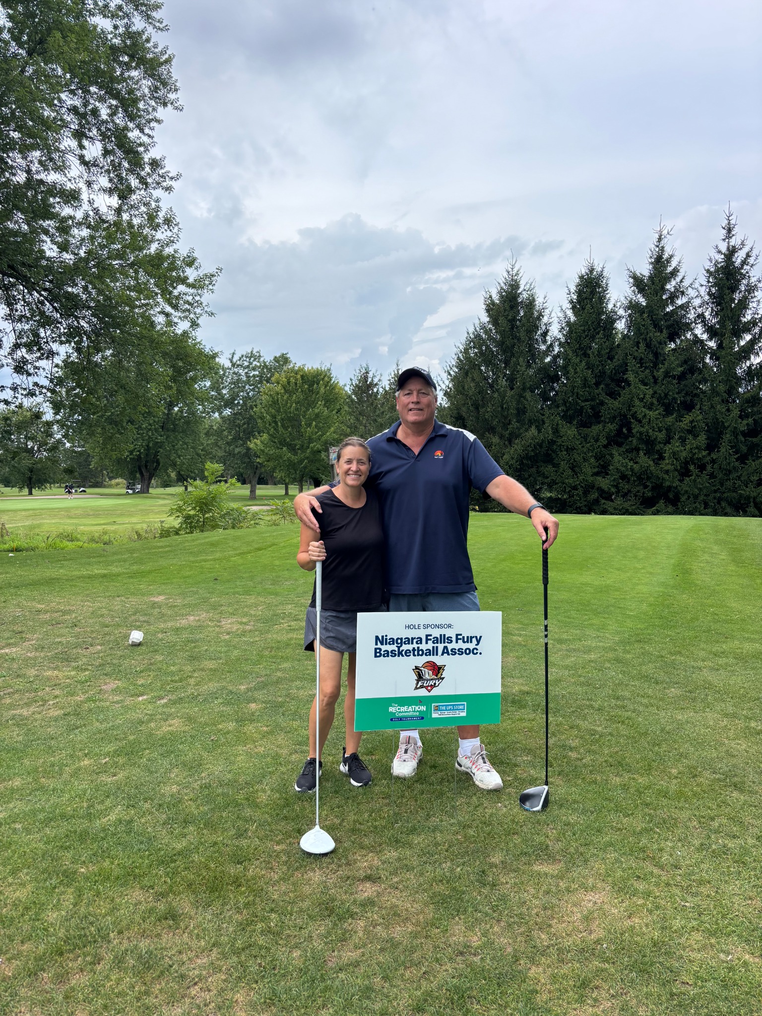Terry at a community golf event beside a Niagara Falls Fury Basketball sign